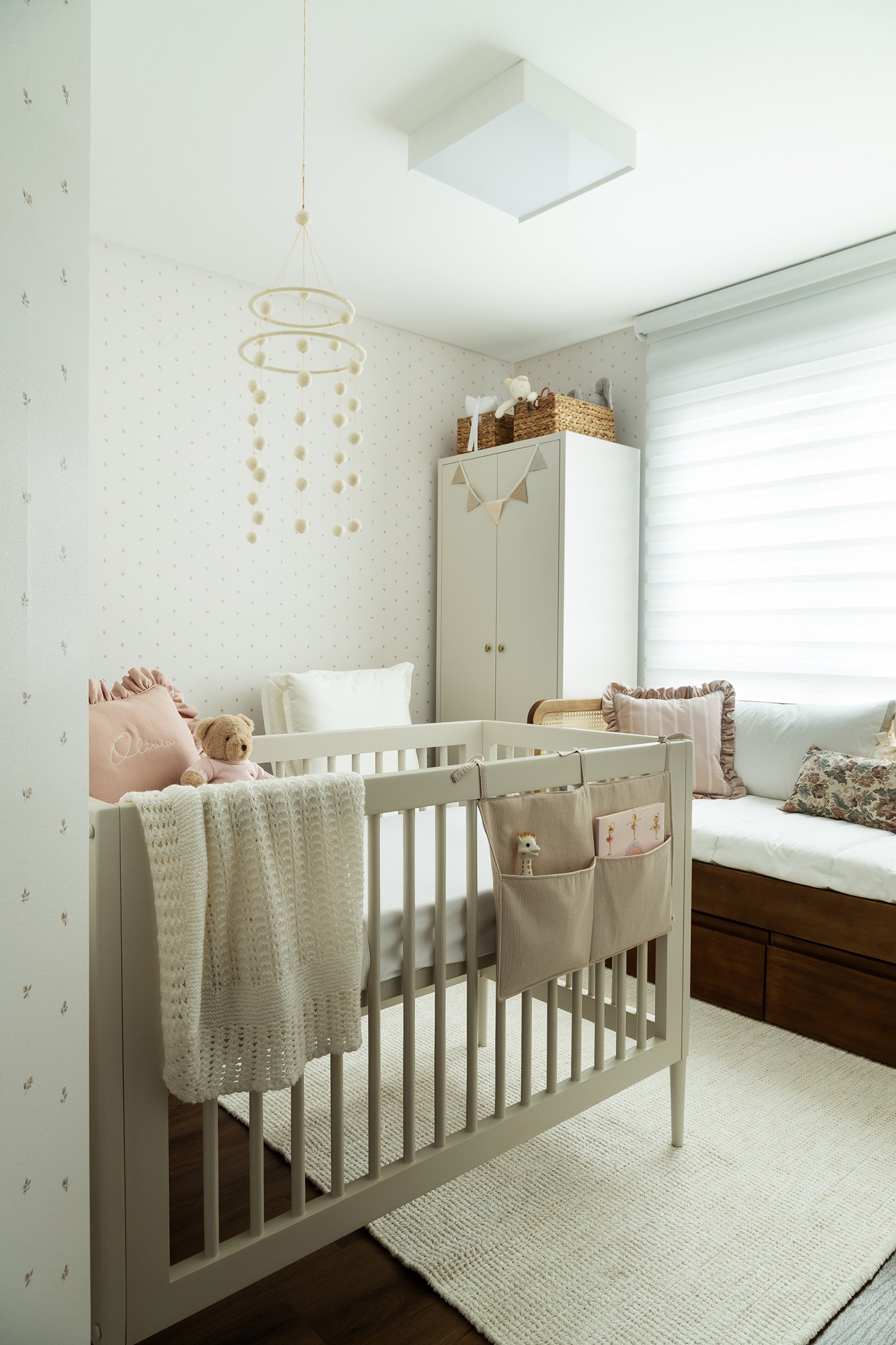 Visão geral de quarto de bebê menina, da pequena Olívia, com berço, armário, cama auxiliar e poltrona de amamentação.