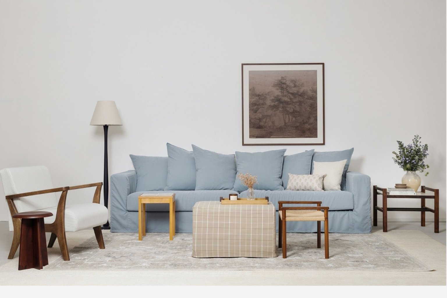 Imagem de uma sala de estar com os principais produtos da nova coleção Casa para ser vivida da Luiza Porto. Conta com itens como a luminária de chão, a poltrona Lila, a mesa lateral Fenda, a mesa em madeira com tampo de azulejos artesanal, a capa para pufe York xadrez, o banco trançado Petit, as capas de almofada Avignon e Bérgamo, e os vasos de cerâmica Chamote e Grés.