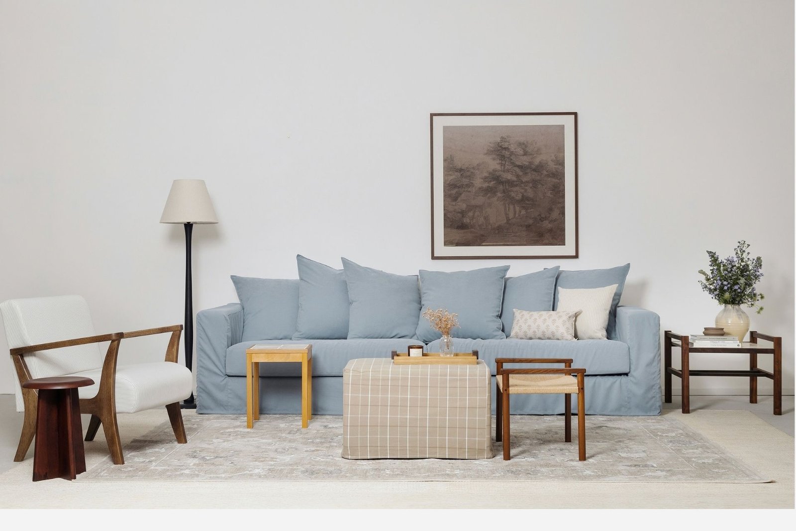 Imagem de uma sala de estar com os principais produtos da nova coleção Casa para ser vivida da Luiza Porto. Conta com itens como a luminária de chão, a poltrona Lila, a mesa lateral Fenda, a mesa em madeira com tampo de azulejos artesanal, a capa para pufe York xadrez, o banco trançado Petit, as capas de almofada Avignon e Bérgamo, e os vasos de cerâmica Chamote e Grés.