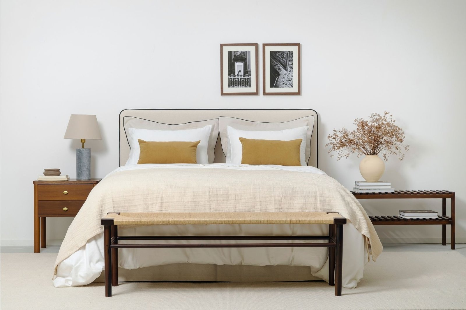 Imagem de um quarto com cama queen, mesas de cabceira e novos produtos da coleção Casa para ser vivida: capa de almofada Siena, vaso de cerâmica Montana, fotografias emolduradas Rosenborg e Hamburgo, cabeceira estofada com rolotê e saia para cama box no mesmo tecido da cabeceira.